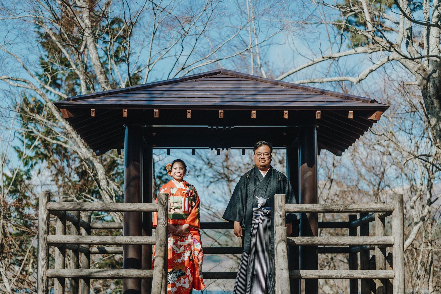 Traditional Japanese wedding photo at a wooden gazebo with mountain views.