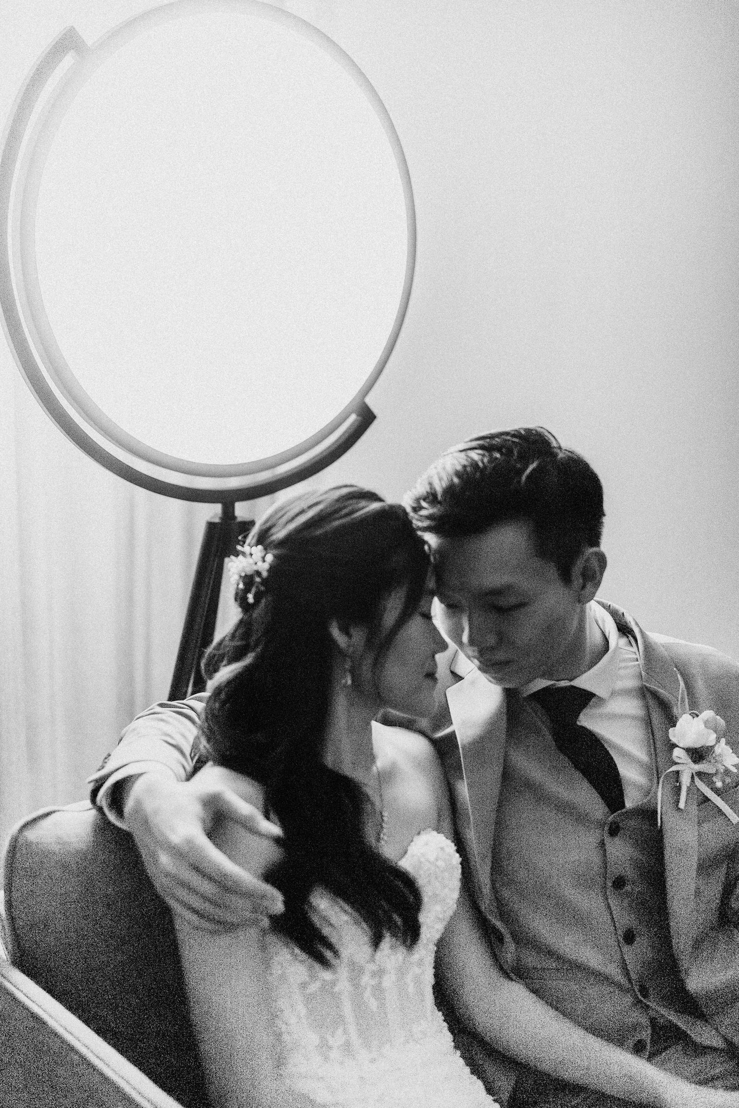 A romantic black and white wedding portrait of a couple sharing an intimate moment near a circular mirror.
