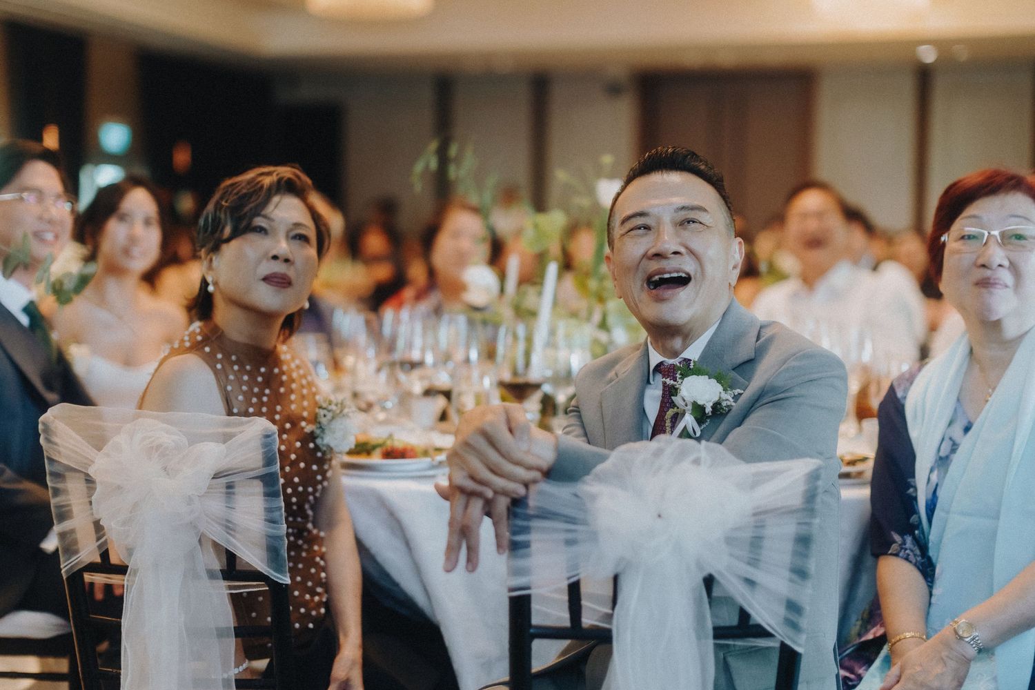 Joyful wedding guests laugh during reception dinner in elegant indoor venue.
