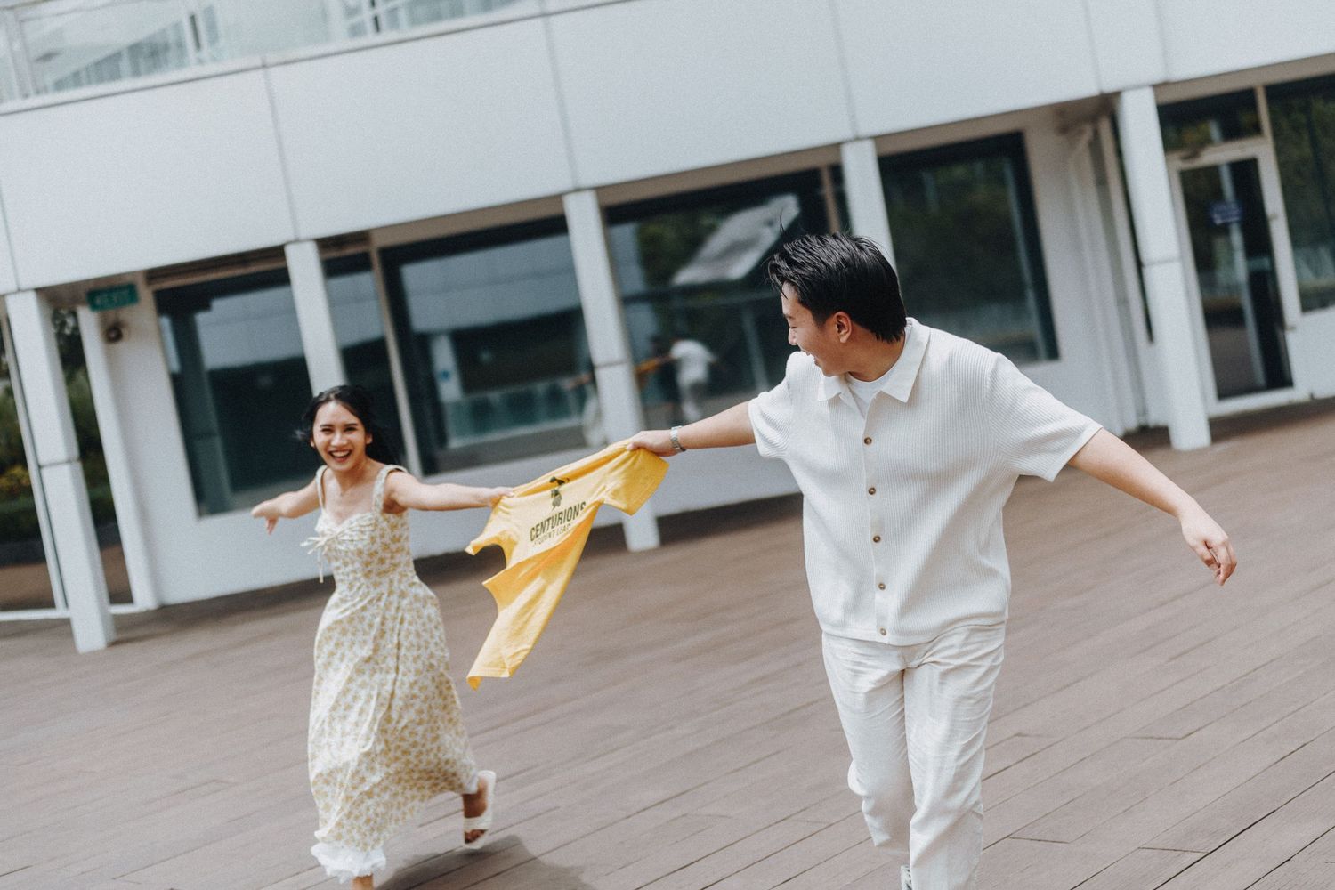 Couple in white outfits dancing and playing on outdoor deck.