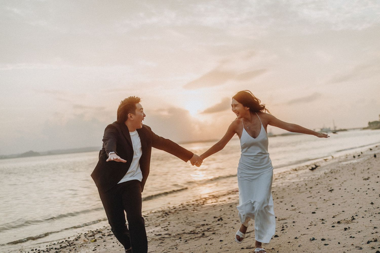 Couple in formal wear walking playfully along beach during golden hour.