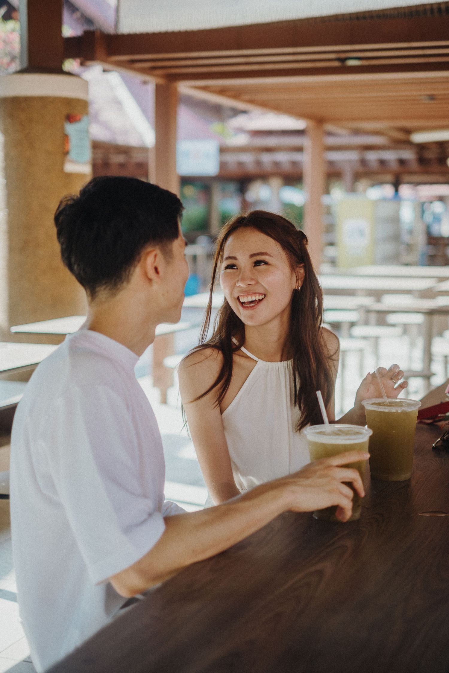 Couple enjoying drinks and conversation at an outdoor cafe with wooden decor.