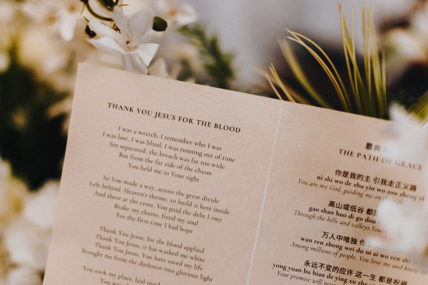 Wedding menu card with English and Chinese text displayed among blurred floral decorations.