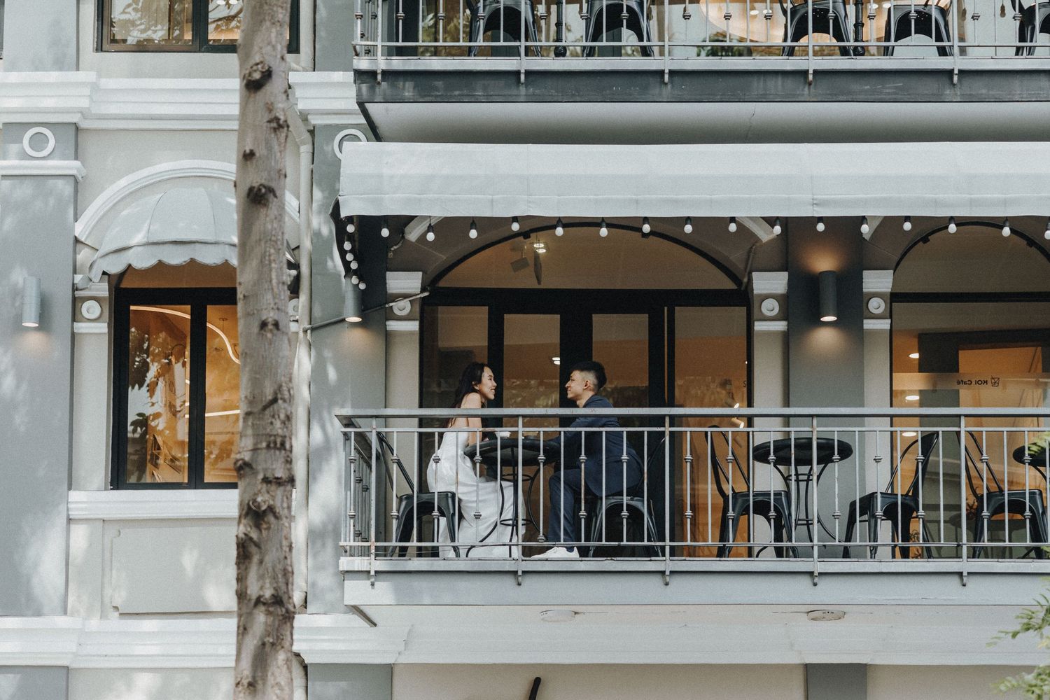 A modern elevated balcony with white railings and columns overlooking a row of trees in an urban setting.