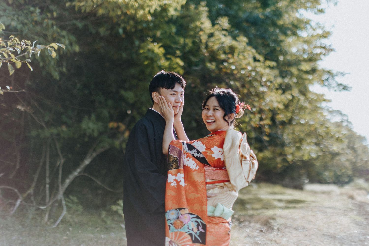A couple in traditional Japanese kimono attire share a tender embrace against a scenic outdoor backdrop.
