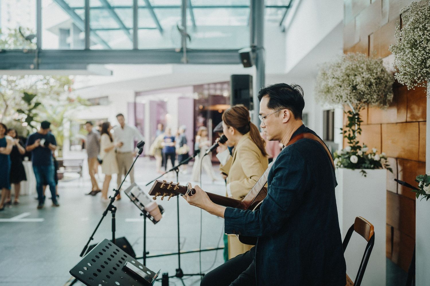 Modern glass wedding venue with scattered guests and photographers capturing moments.