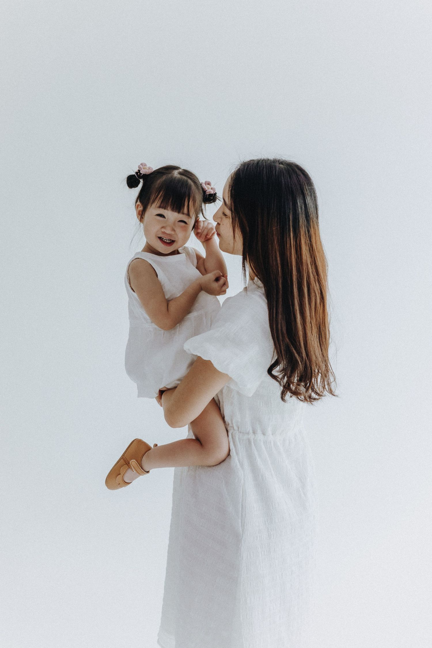 A tender mother and child moment wearing all white against a minimalist background.