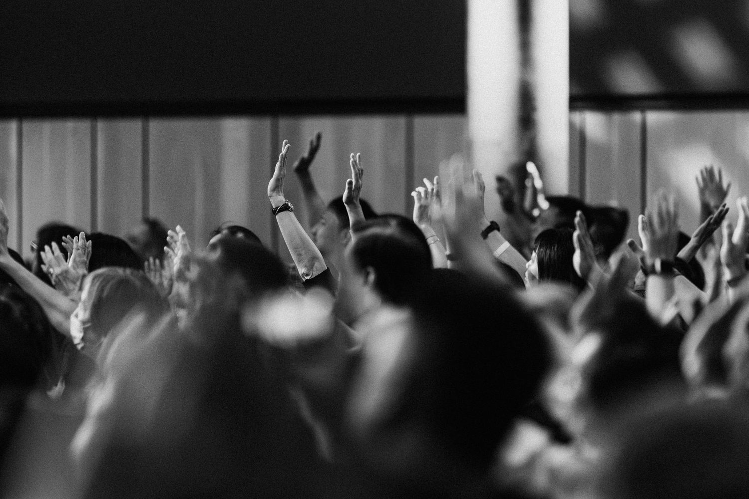 Concert crowd at nighttime raises their hands in excitement as bright stage lights illuminate the dark venue.