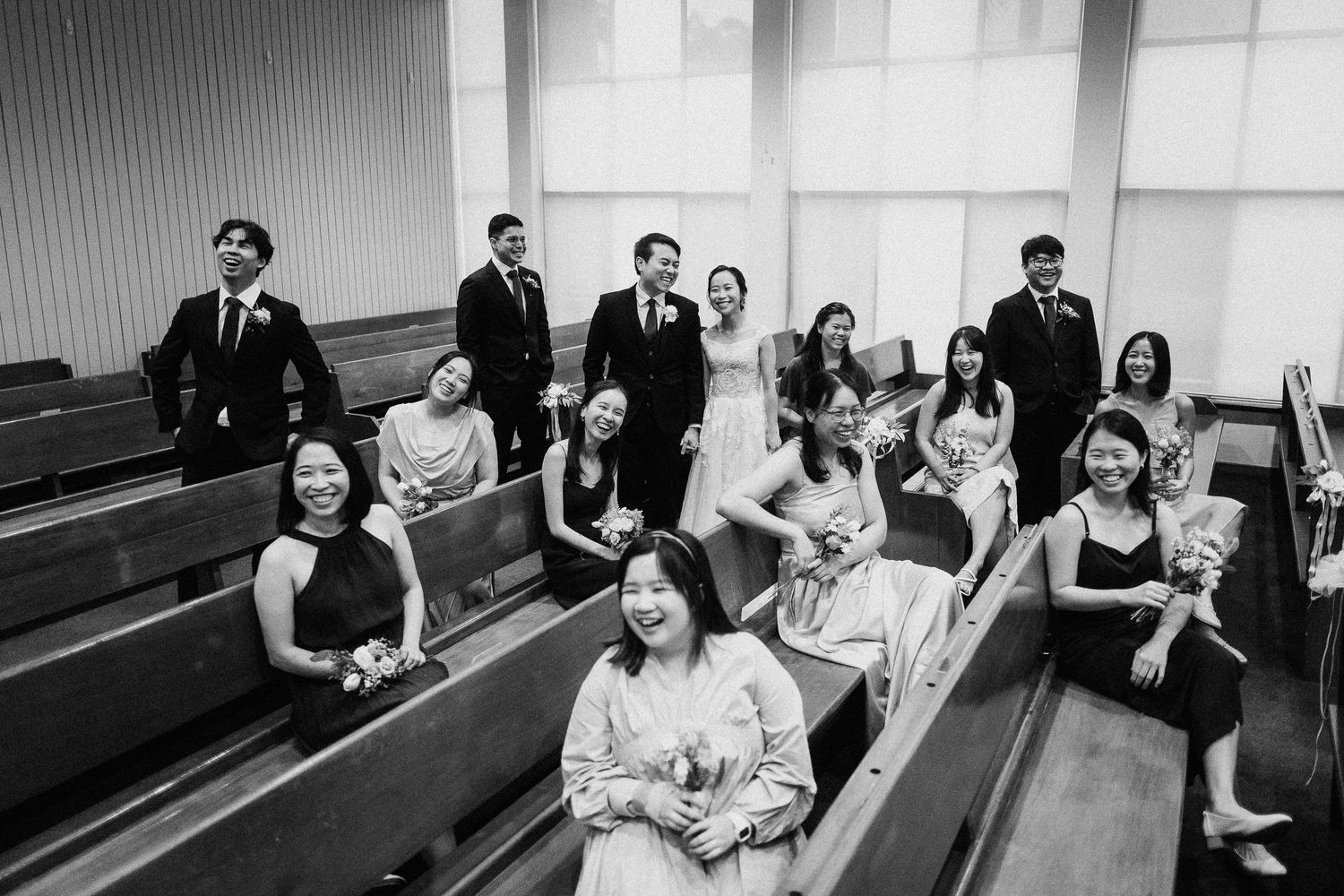 Guests seated in wooden church pews at a formal ceremony with people standing in the aisle in black and white photograph.