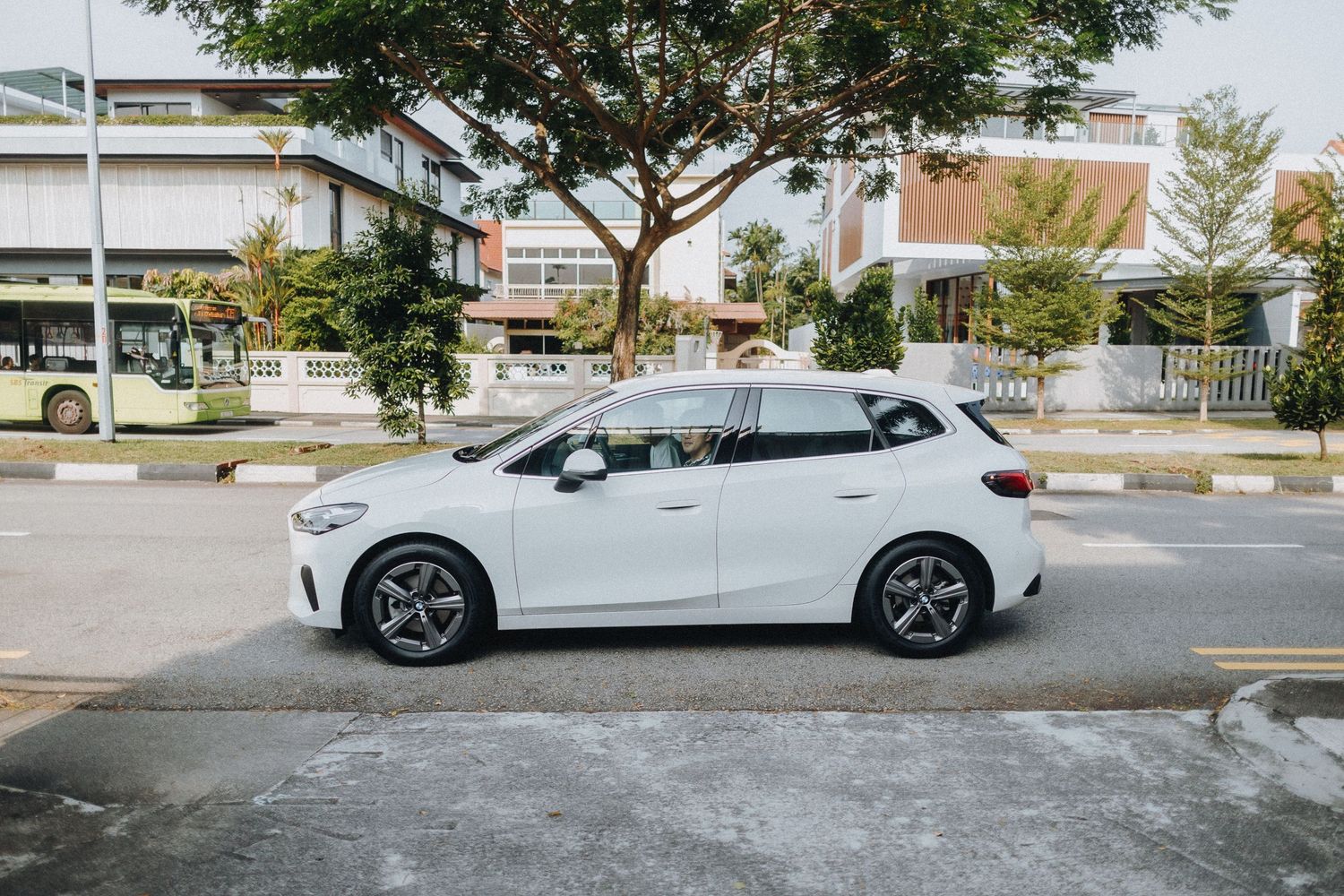 A white electric car is parked in a parking lot near trees and buildings on a sunny day.