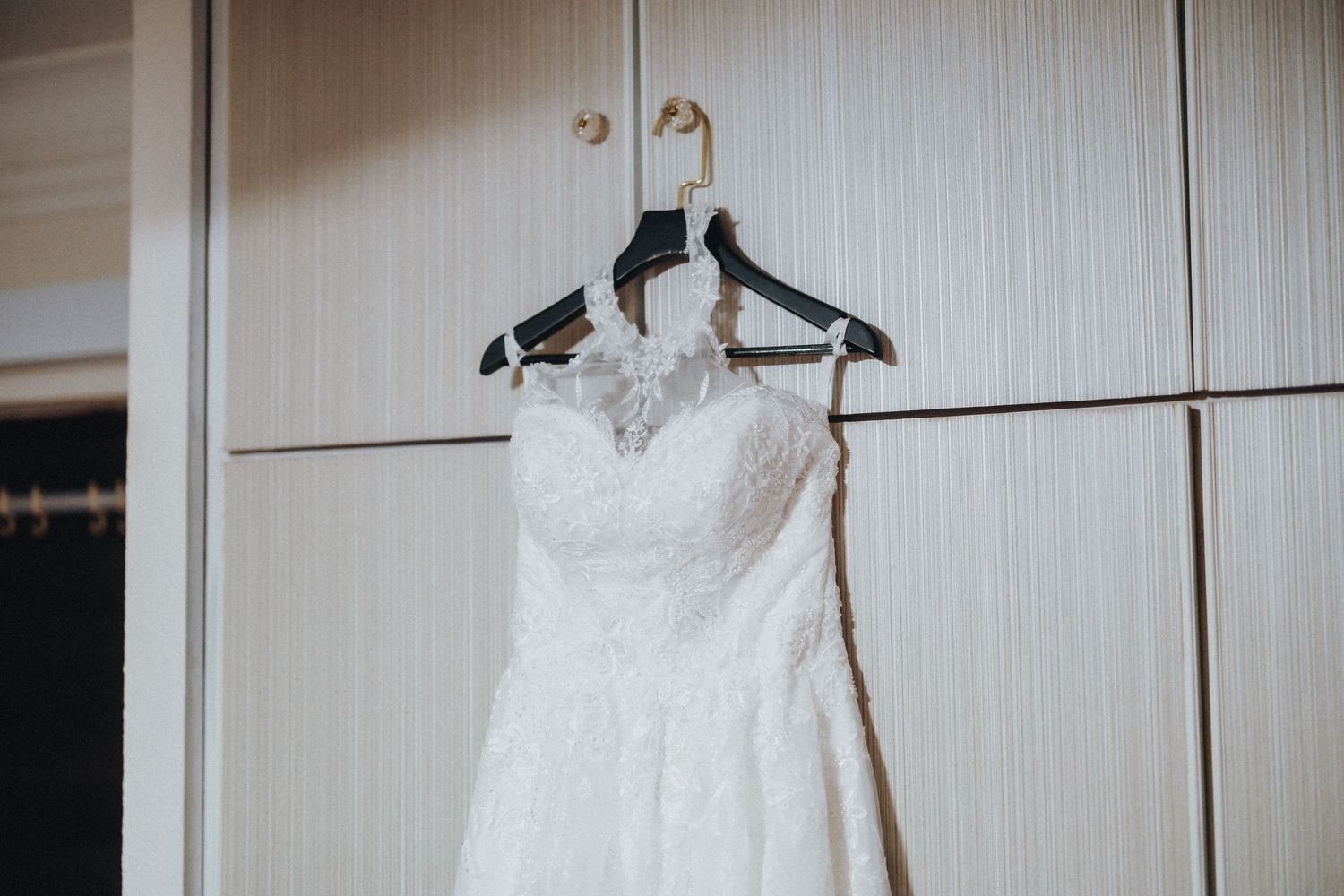 Wedding dresses displayed on hangers against a white wall in a bridal boutique.