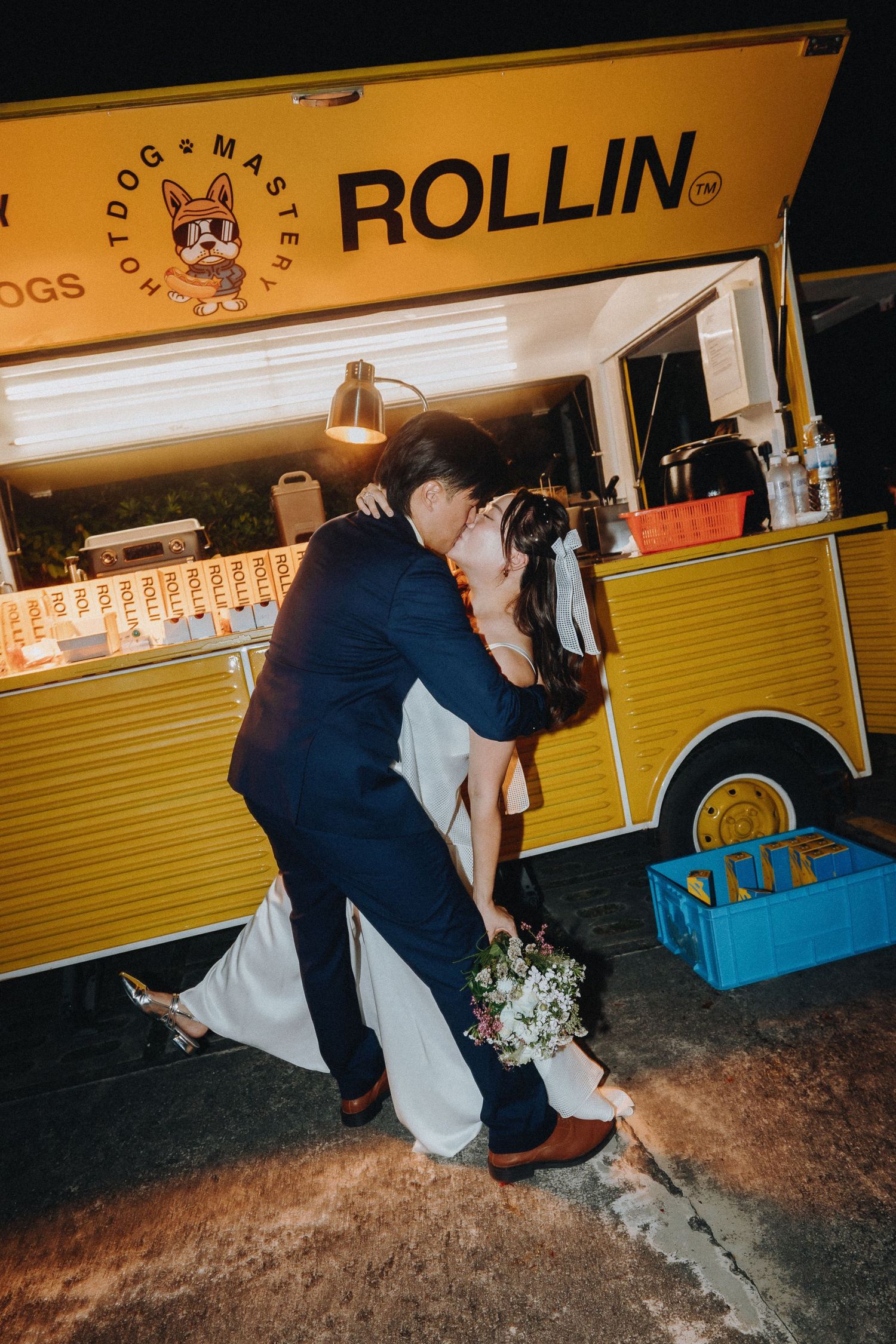 Romantic dip kiss between newlyweds in front of a yellow food truck at night.