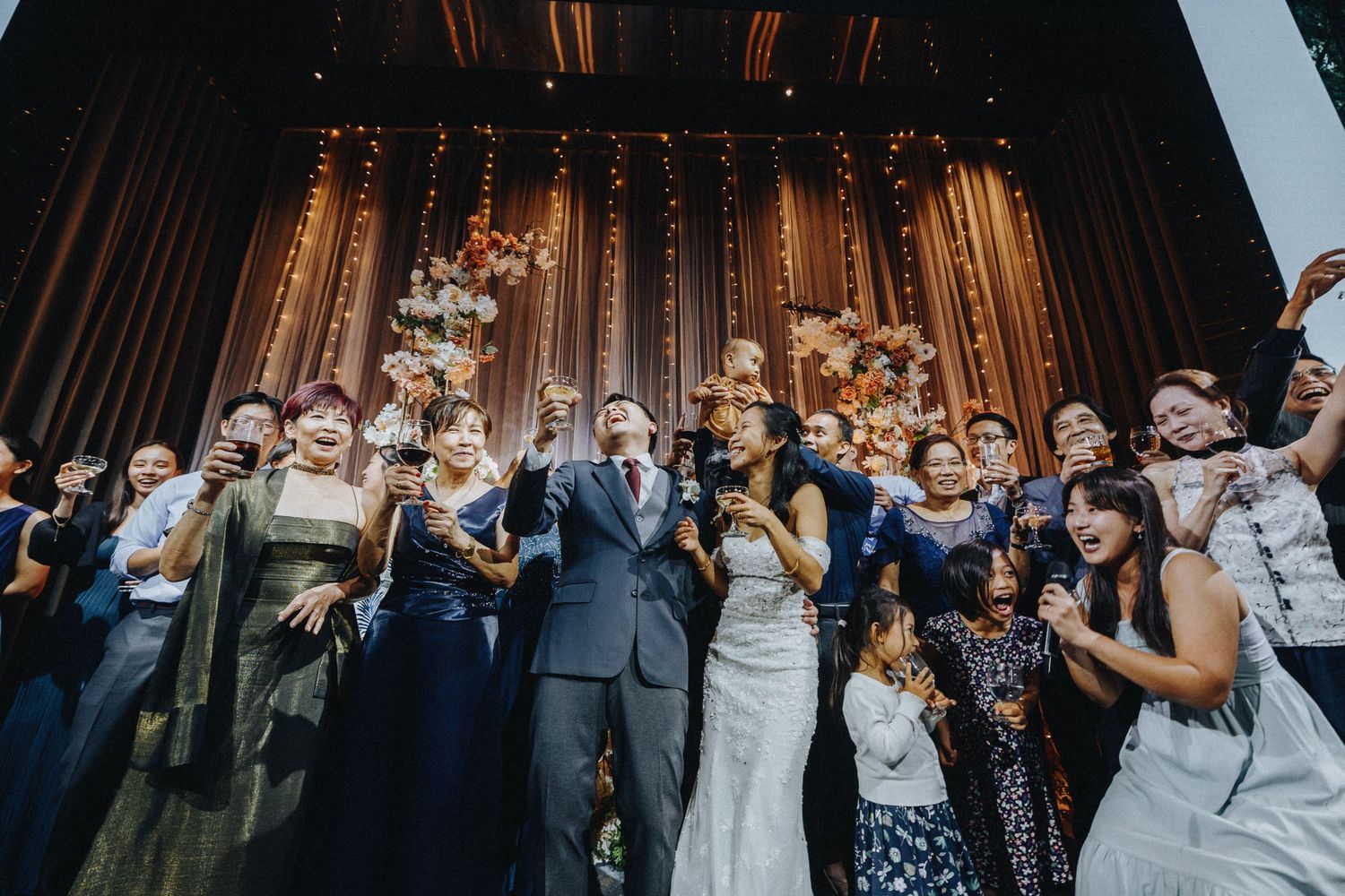 Wedding celebration with large group gathered on stage under dramatic lighting during reception party.
