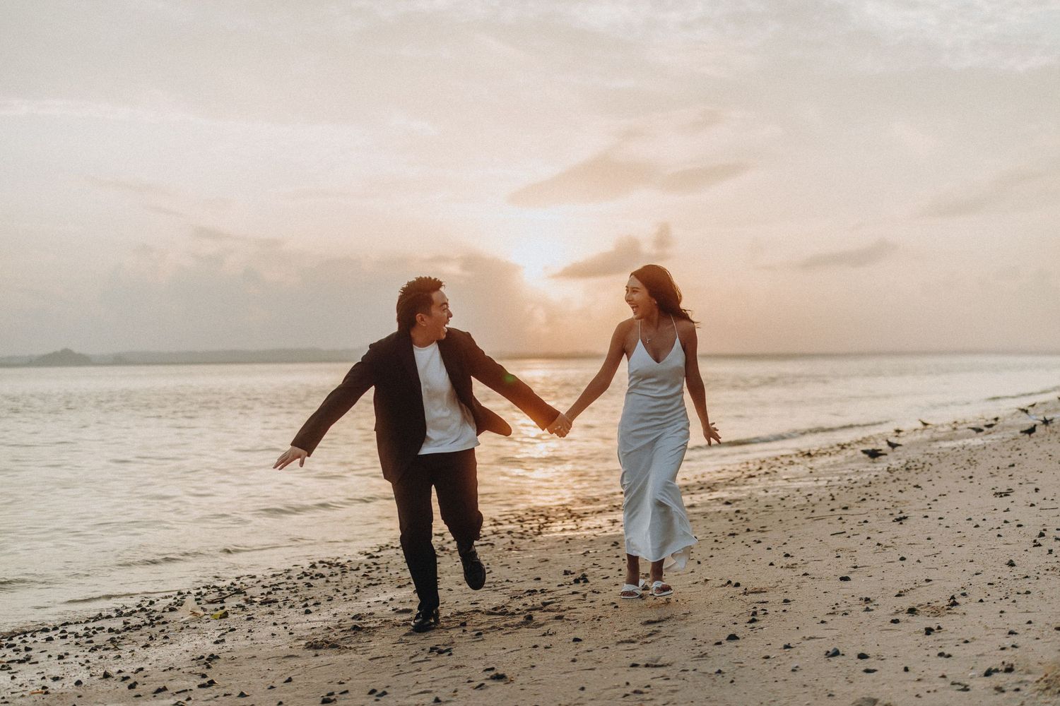 Couple holding hands while walking along rocky beach shoreline at dusk.