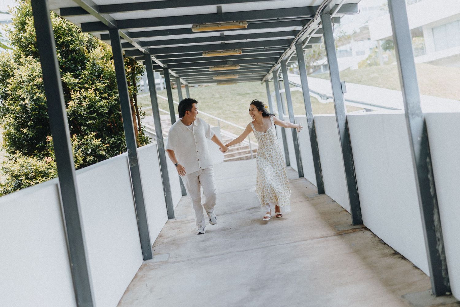 Couple holding hands while walking through covered outdoor hallway in bright daylight.