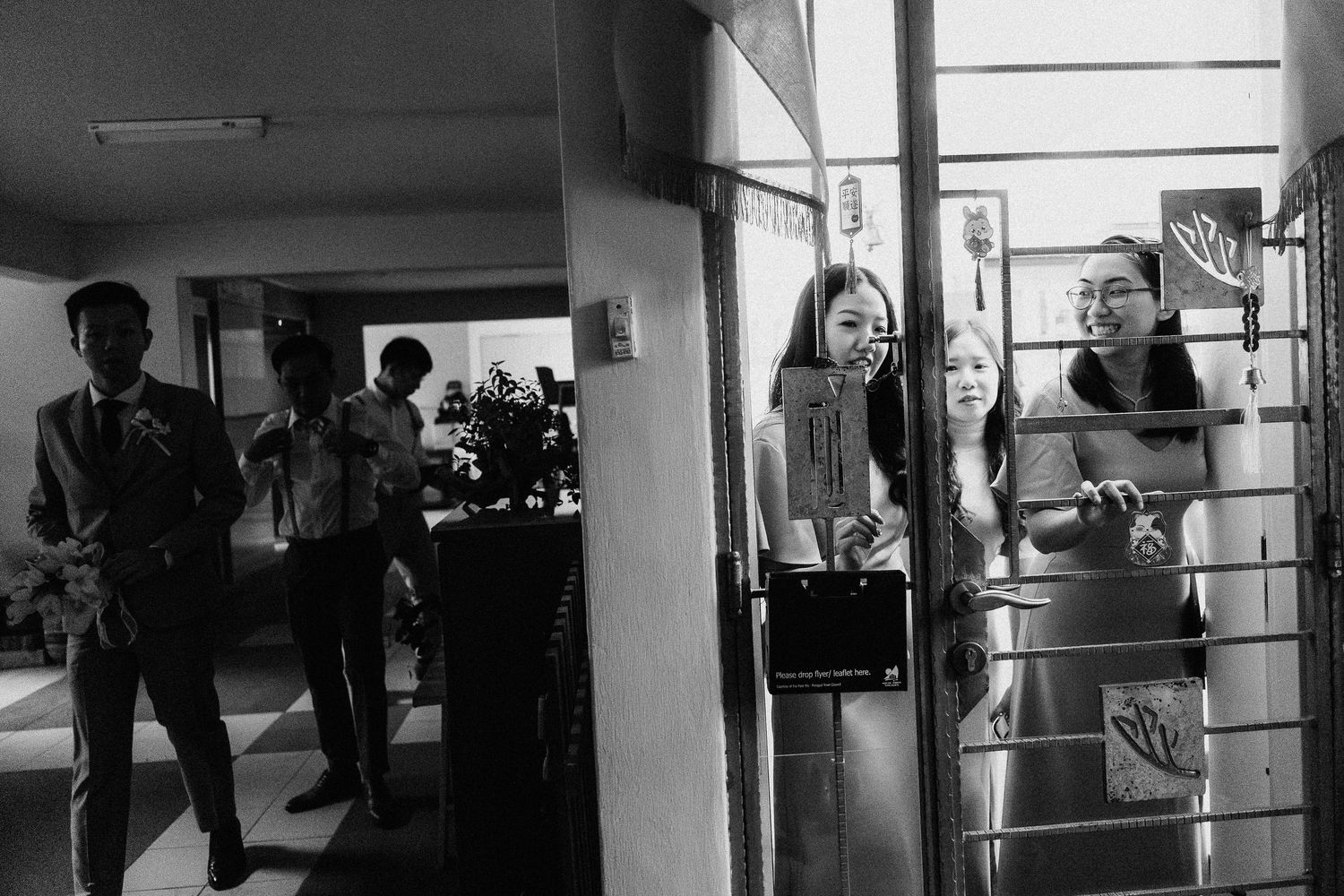 A black and white candid photo of wedding guests gathered in a hallway.