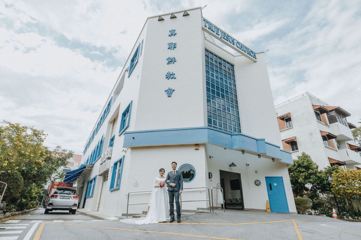 Wedding couple posing outside blue and white church building.