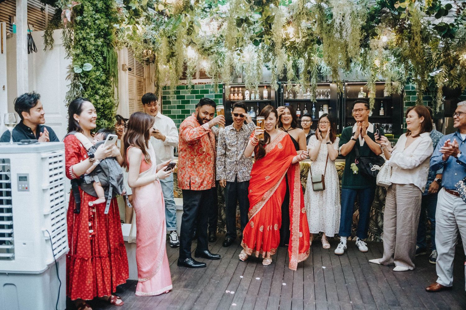 Wedding guests in colorful sarees and traditional attire celebrate together on a decorated outdoor terrace.