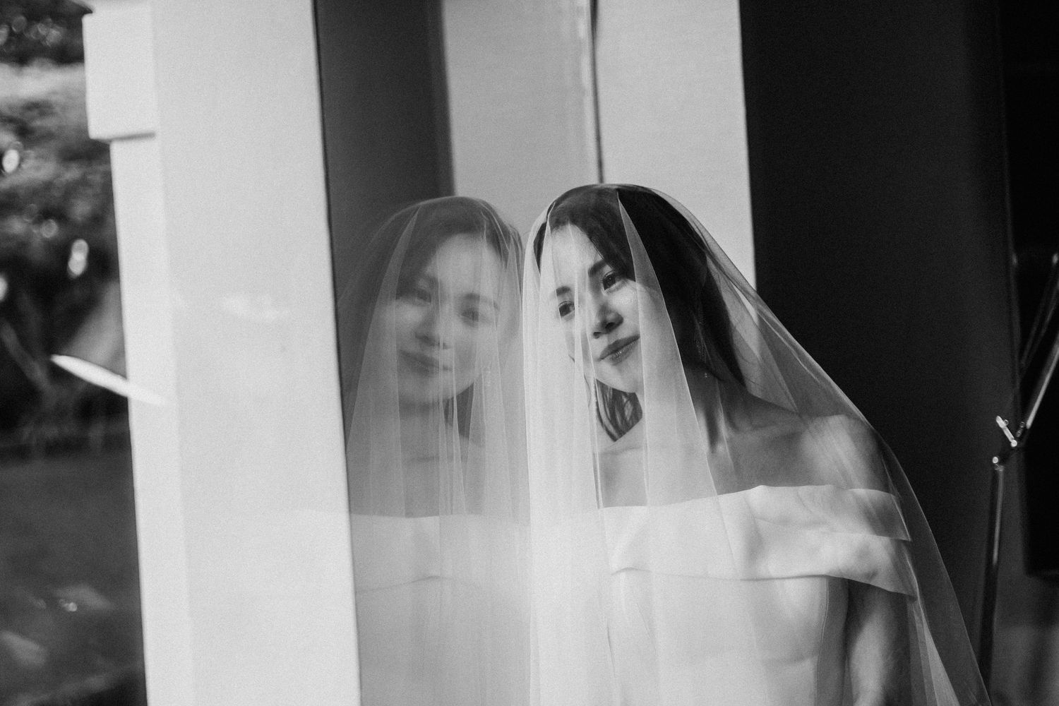 A double exposure black and white bridal portrait showing ethereal reflection through a wedding veil.