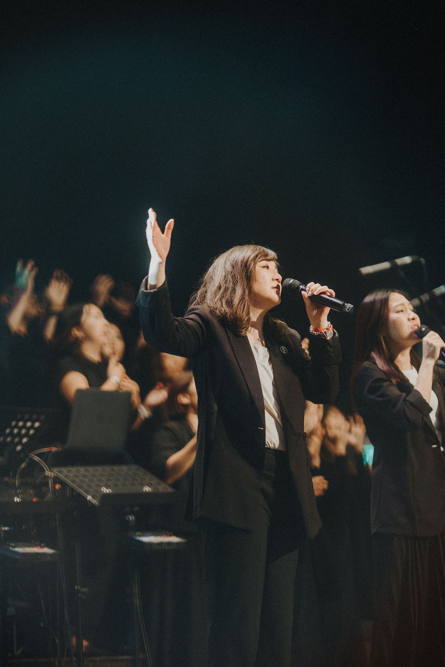 A row of performers in black outfits singing on stage with dramatic lighting and microphones during a musical performance.