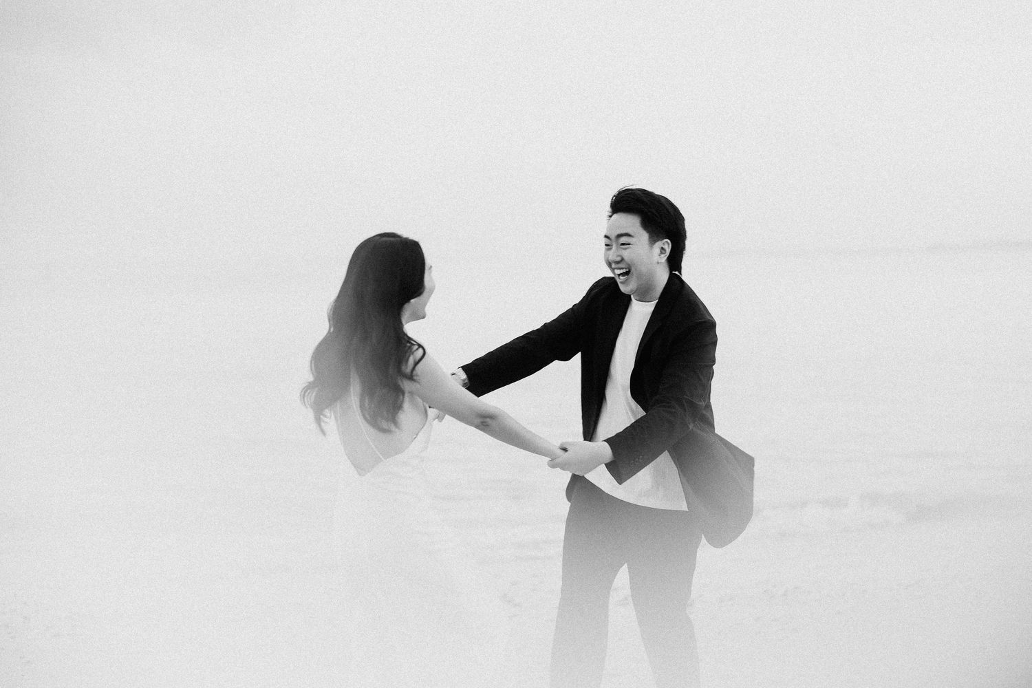Silhouetted couple twirling and dancing together on a serene beach at dusk.