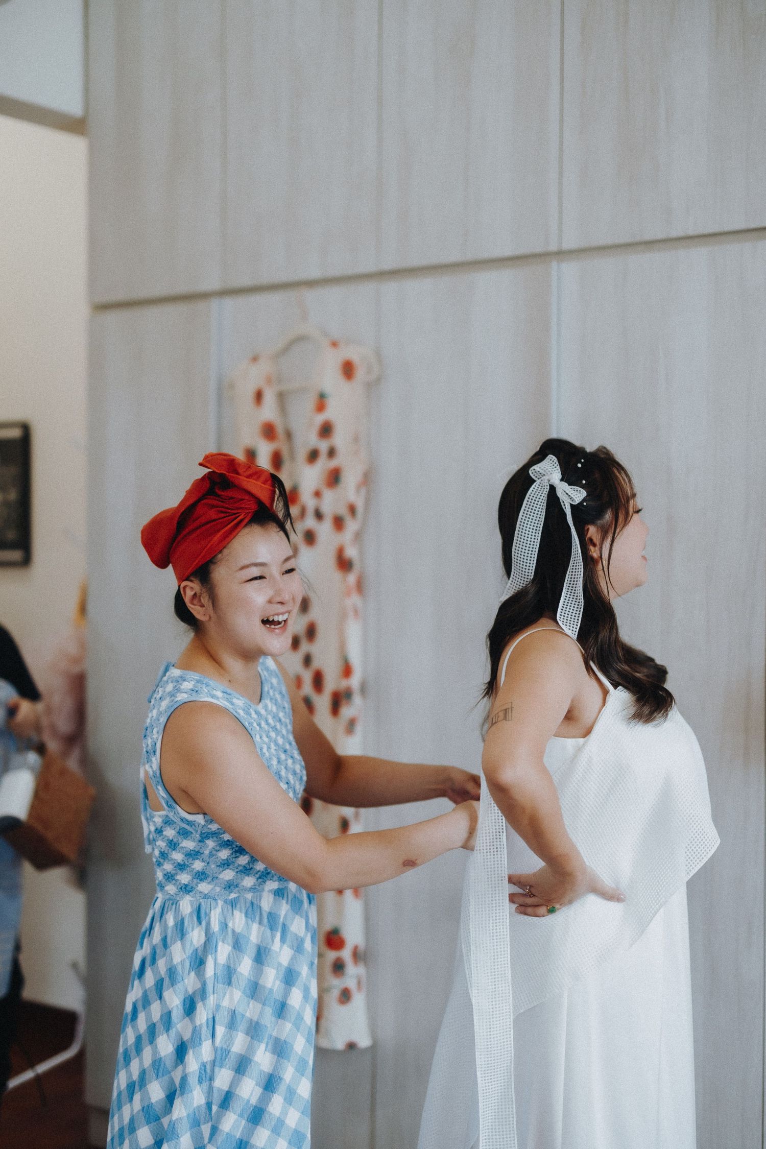 Two people sharing a joyful moment while getting ready in white and blue checkered dresses.
