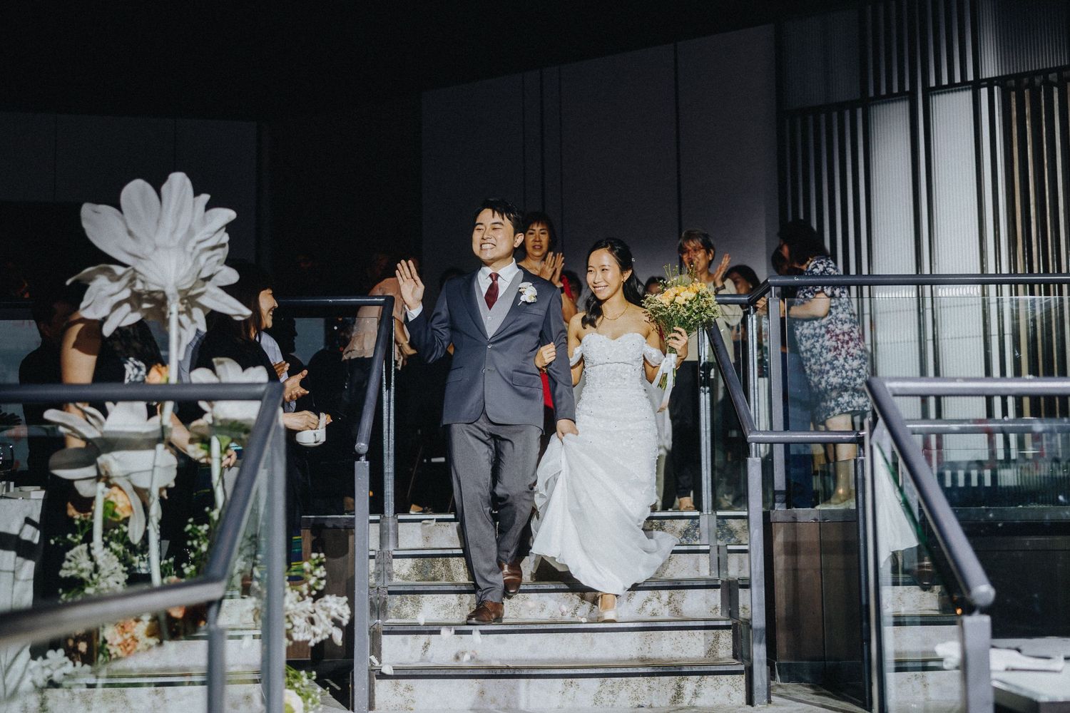 Wedding party and guests celebrating on minimalist stairs in modern architectural setting.