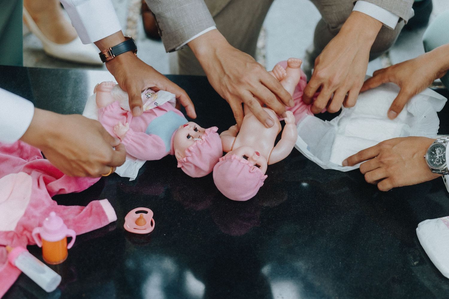 Hands gather around a table arranging small pink piggy banks and various items during a group activity.