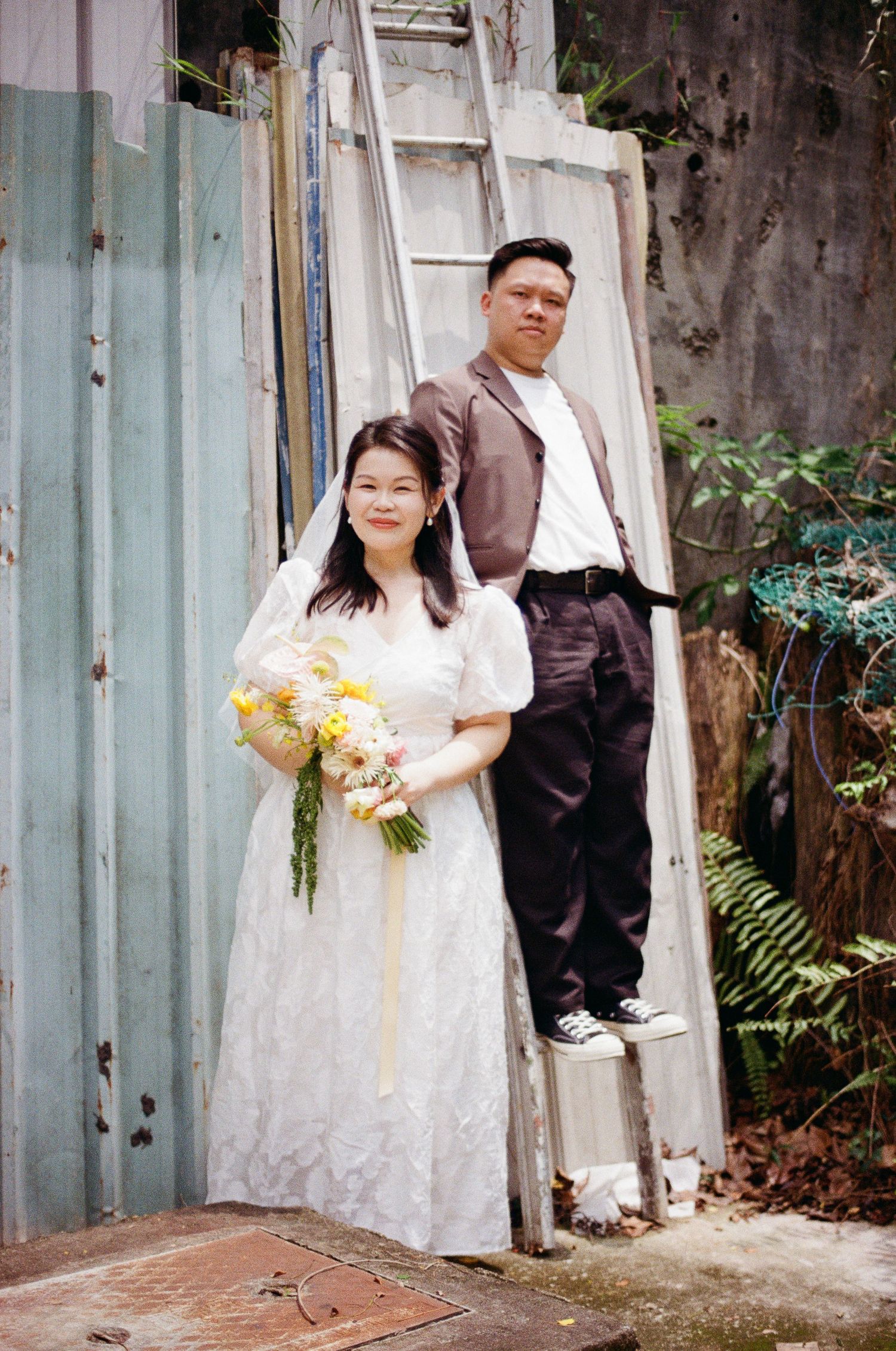 Multiple candid shots of person in white lace dress with yellow bouquet against rustic industrial backdrop.