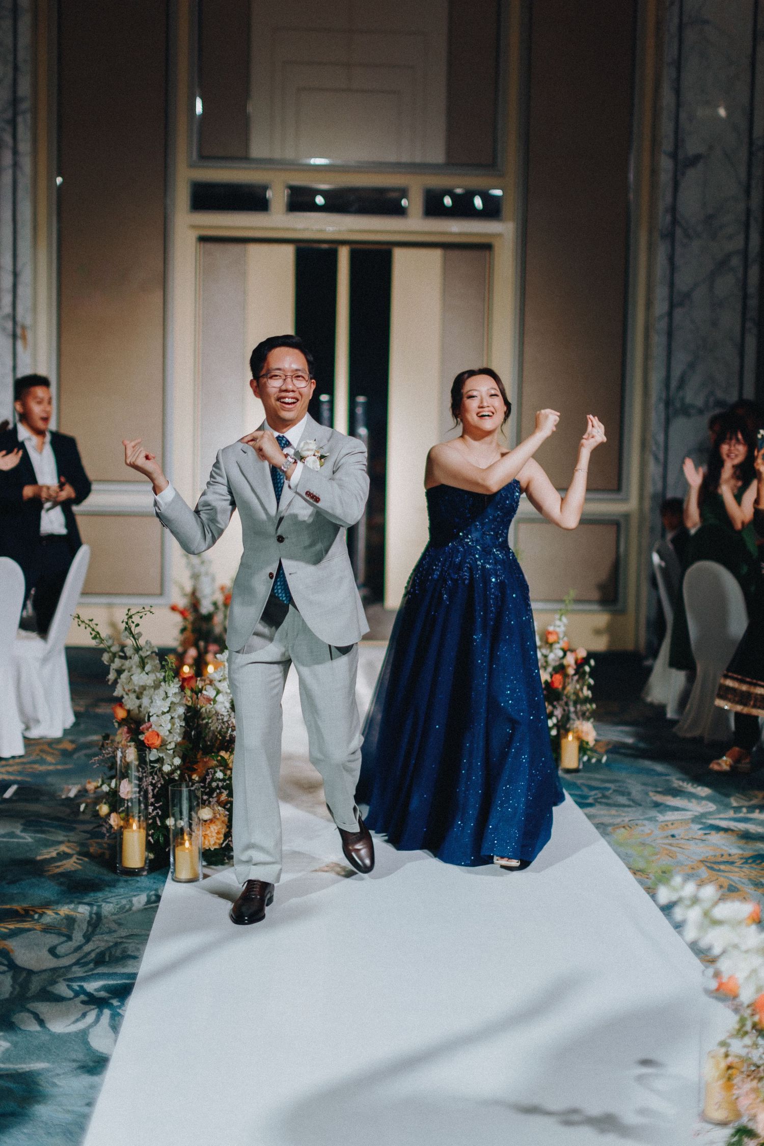 Wedding couple dances joyfully in an elegant ballroom with decorative floral arrangements.