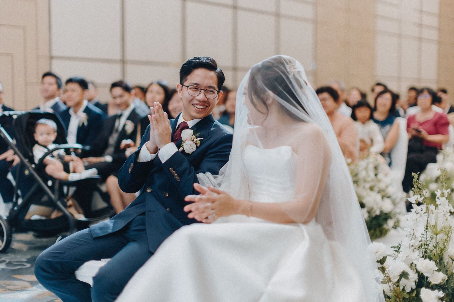 A wedding ceremony moment captured in an elegant ballroom with white floral decorations.