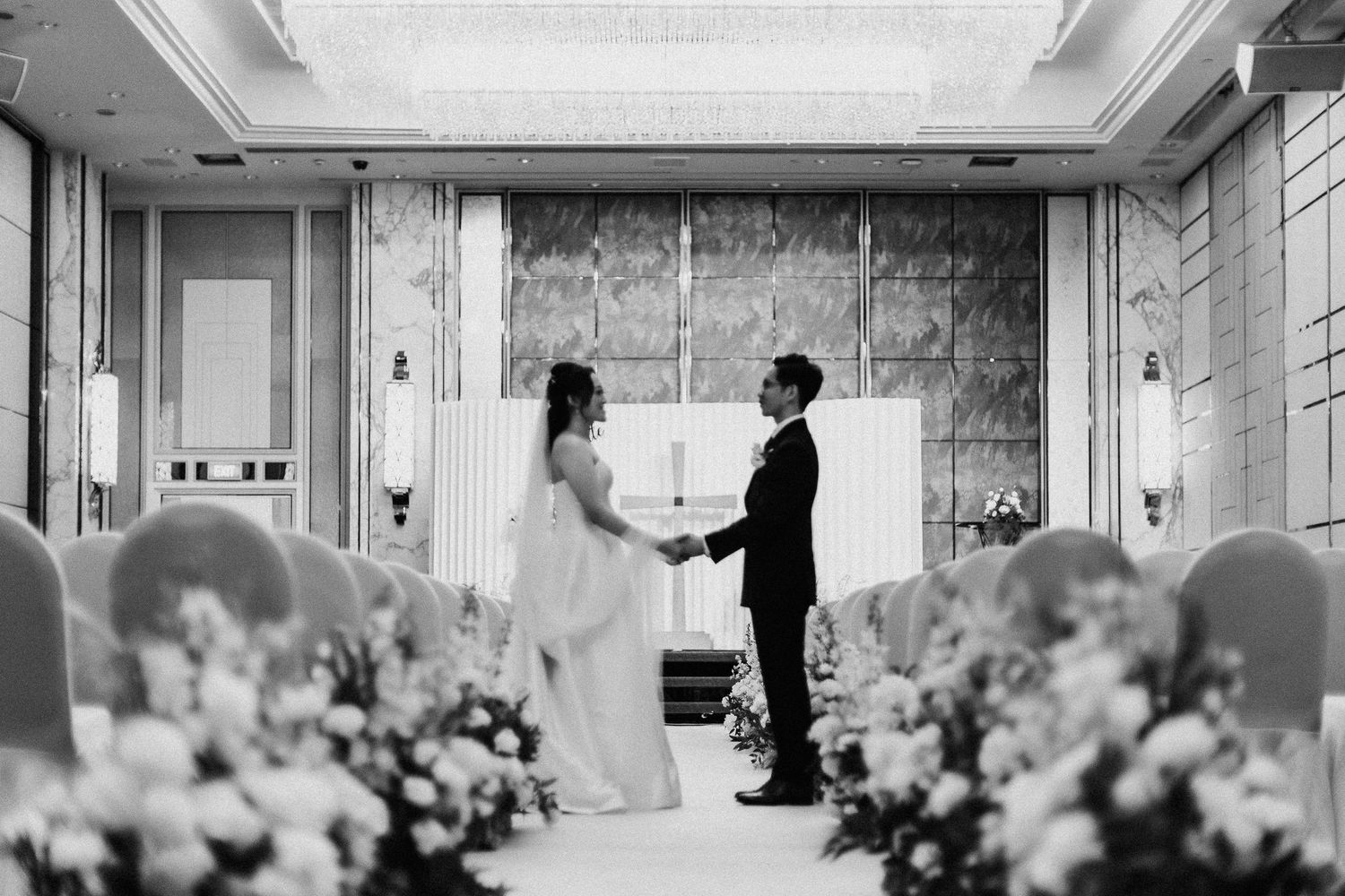A black and white photo of a wedding ceremony with floral decorations and a couple standing at the altar.
