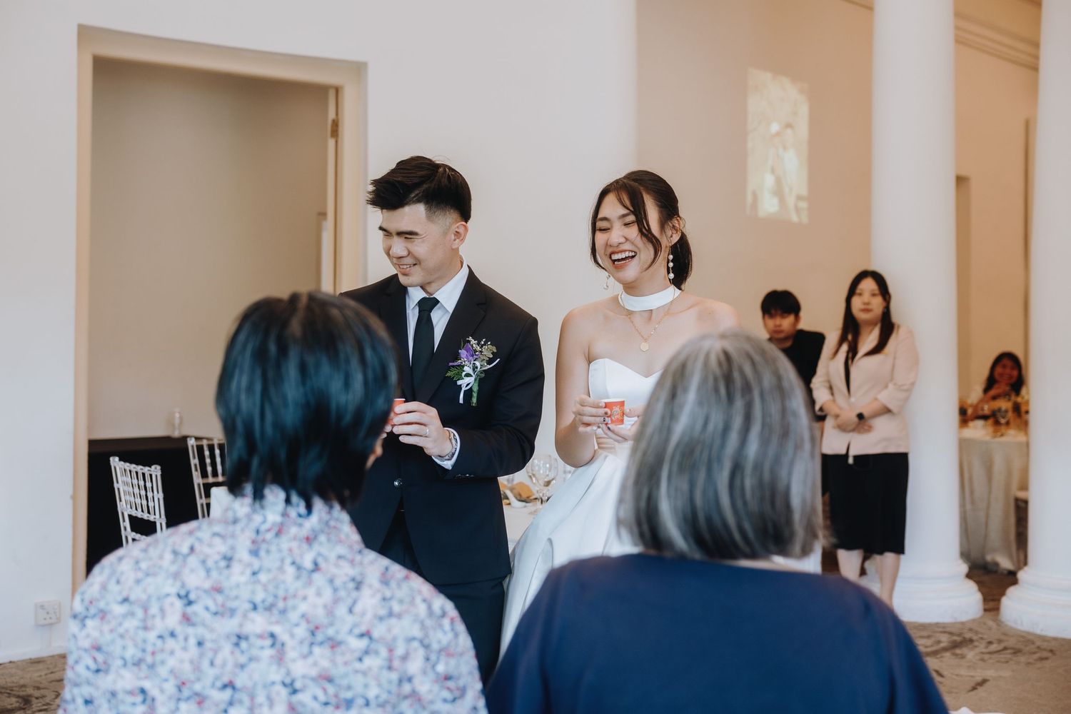 Laughing bride and groom greet elderly guests during their elegant wedding reception.