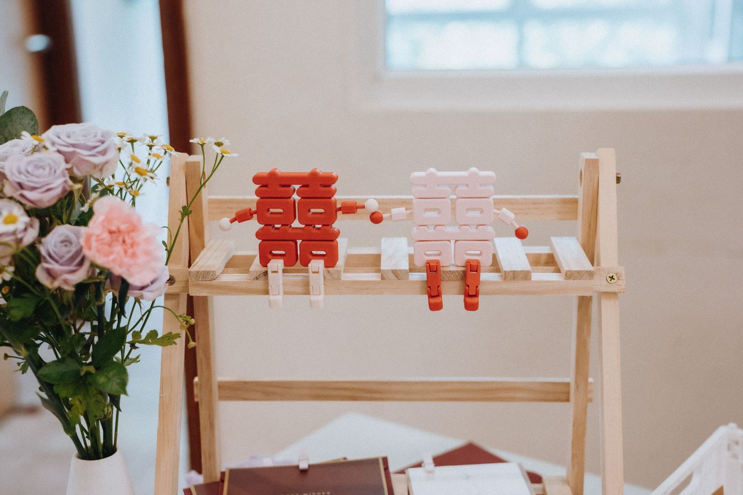 Decorative Chinese double happiness wedding favors displayed on a wooden ladder shelf with flowers.