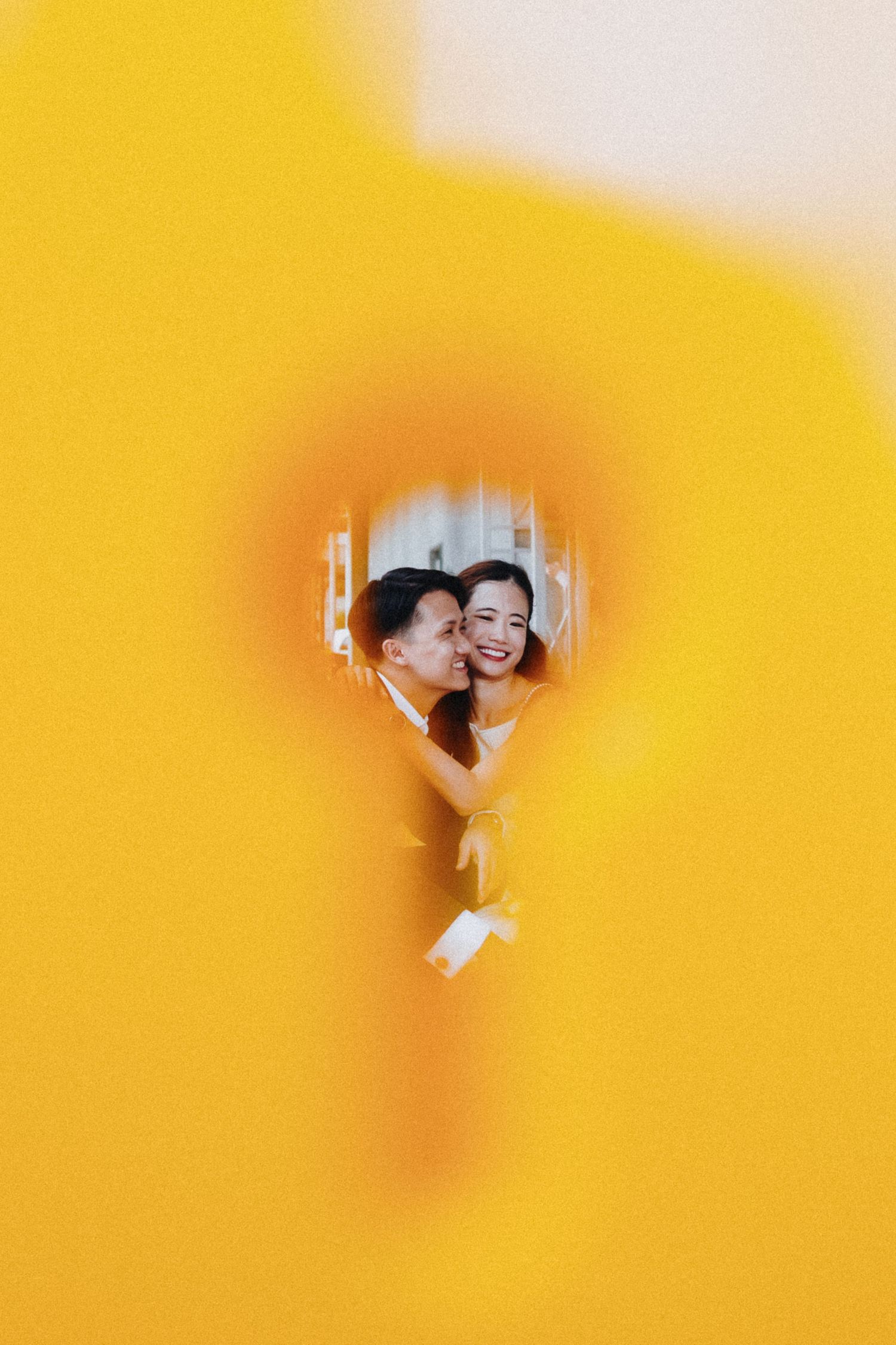 A heart-shaped window in yellow wall frames a candid laughing moment.