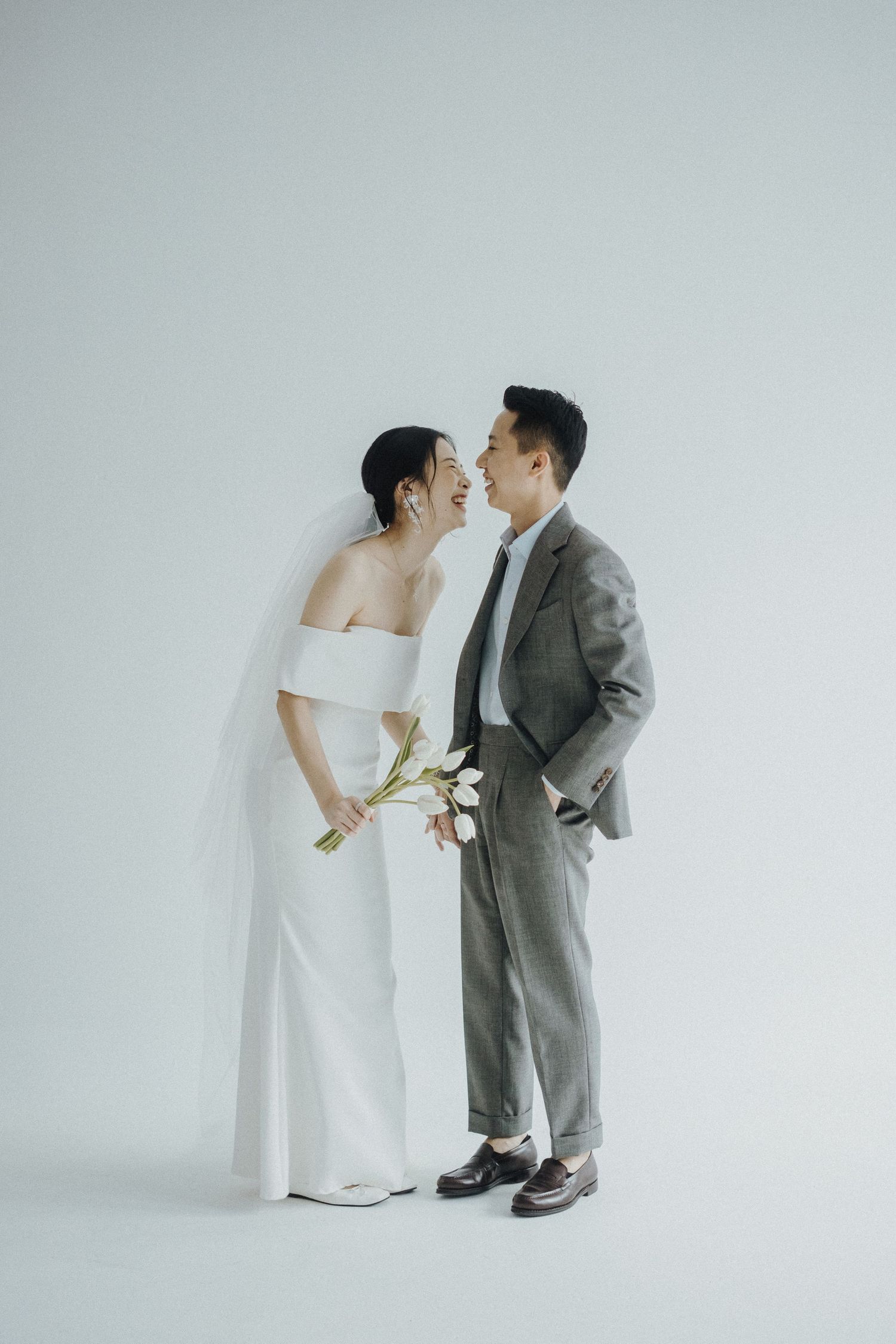 A minimalist wedding photo with a couple in elegant attire standing against a light gray background.