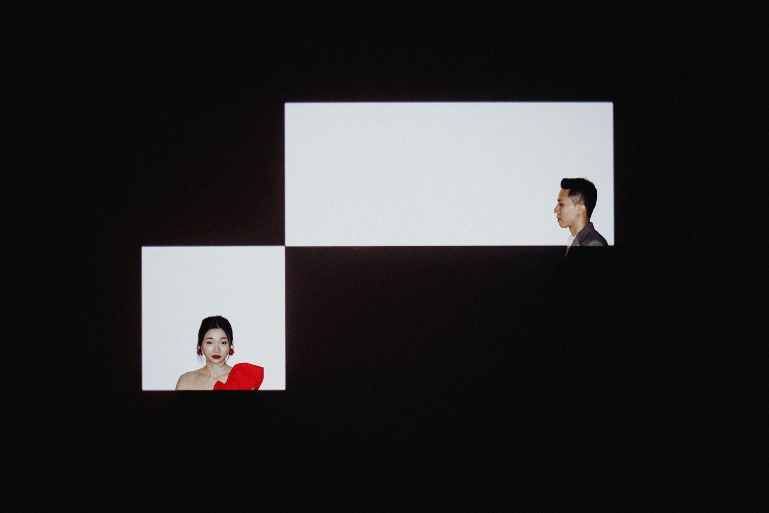 Minimalist composition showing two diagonal white squares with silhouettes against black background.