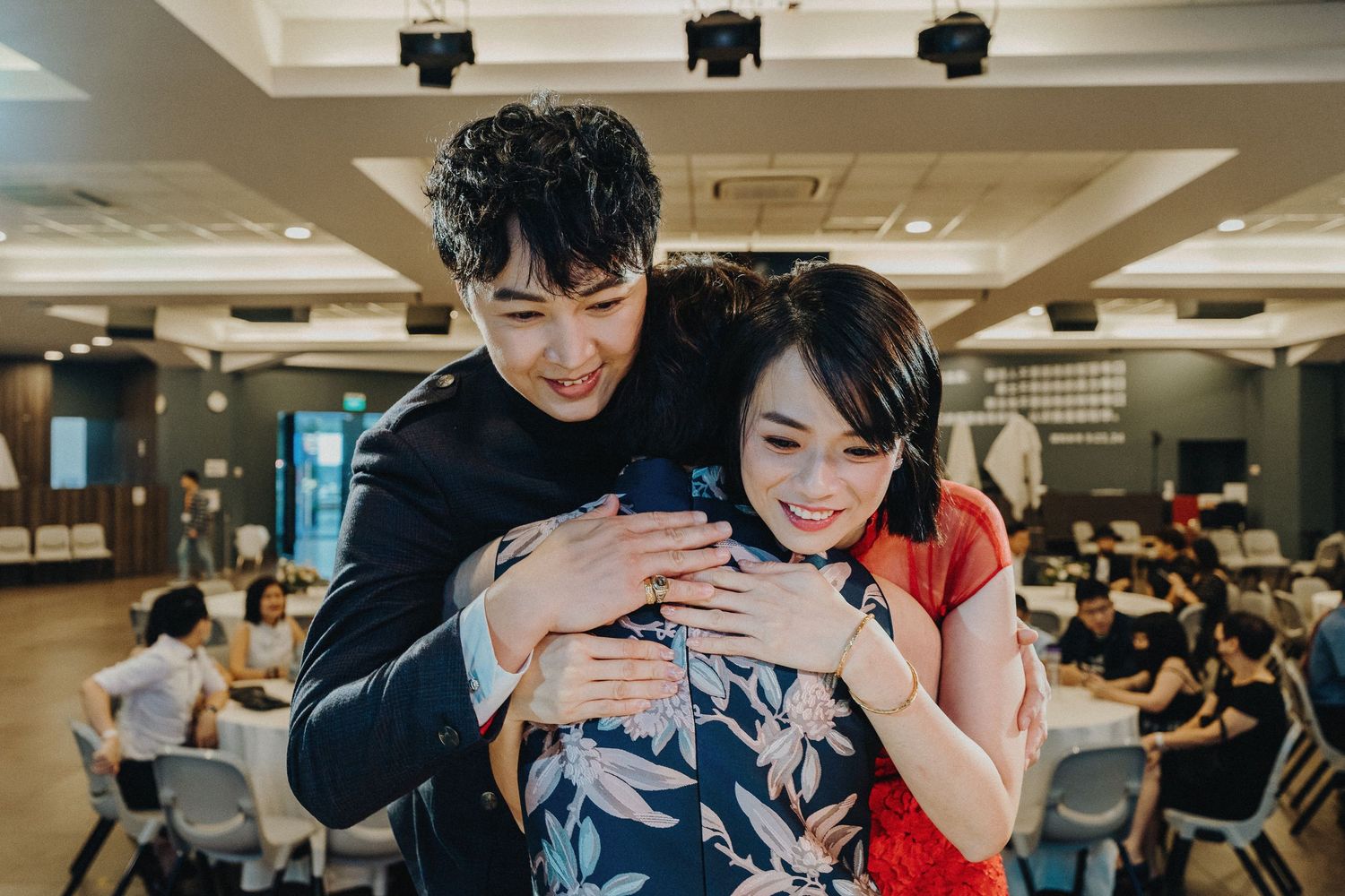 Two people sharing a happy moment together in a casual indoor space with other people seated in the background.