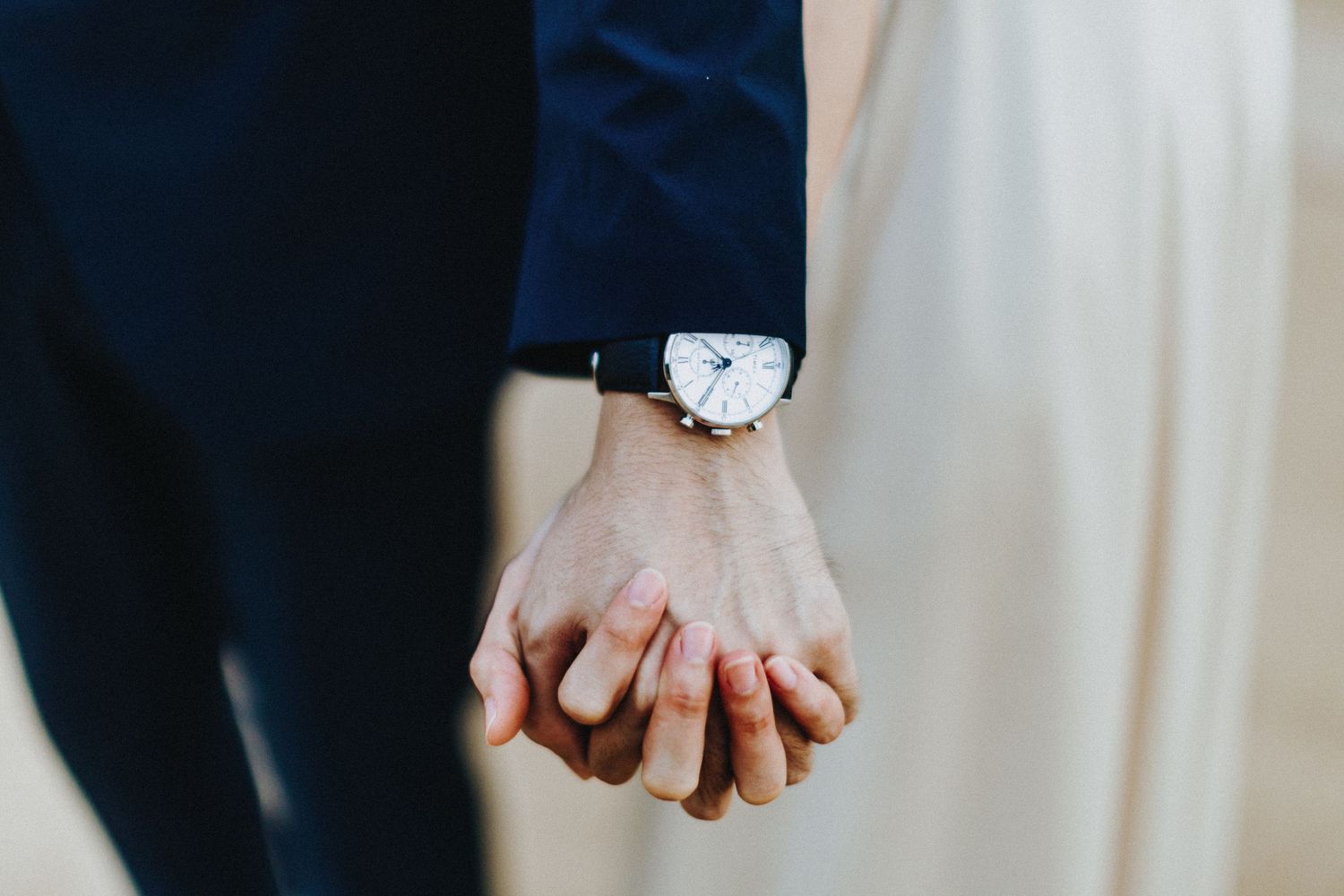 Two hands with wedding rings clasped together affectionately against a light colored background.
