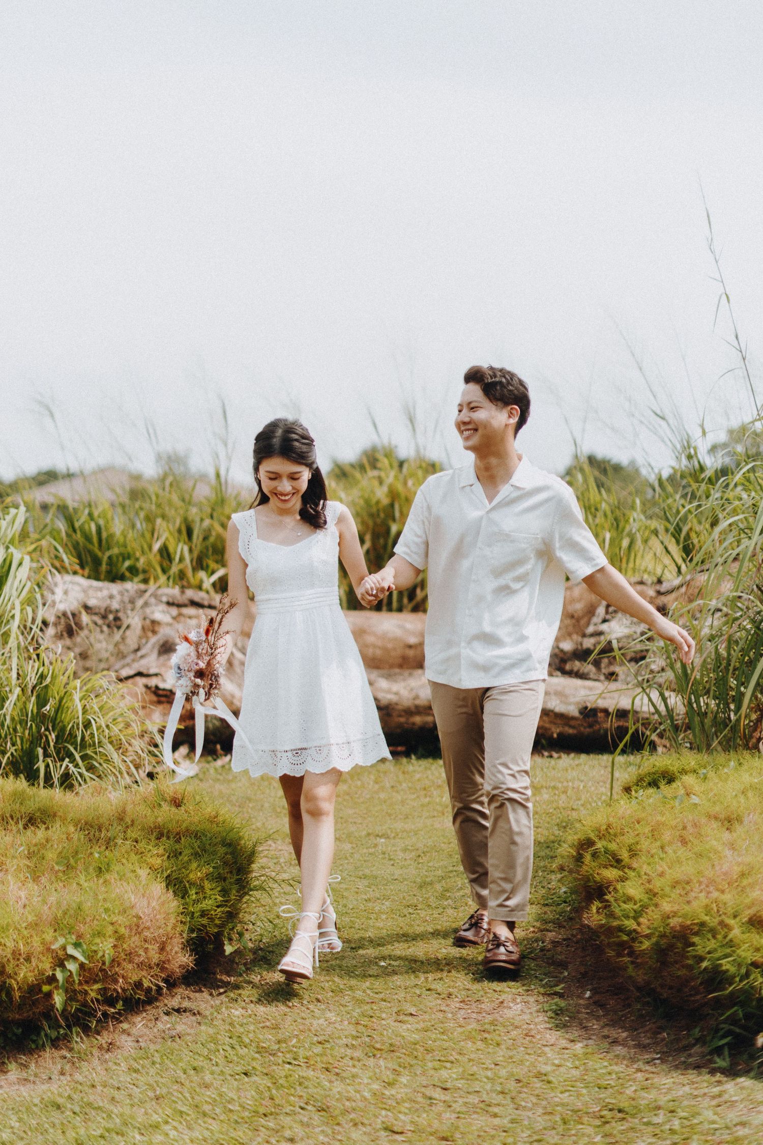 Couple walking together through a grassy field during an outdoor engagement photo session.