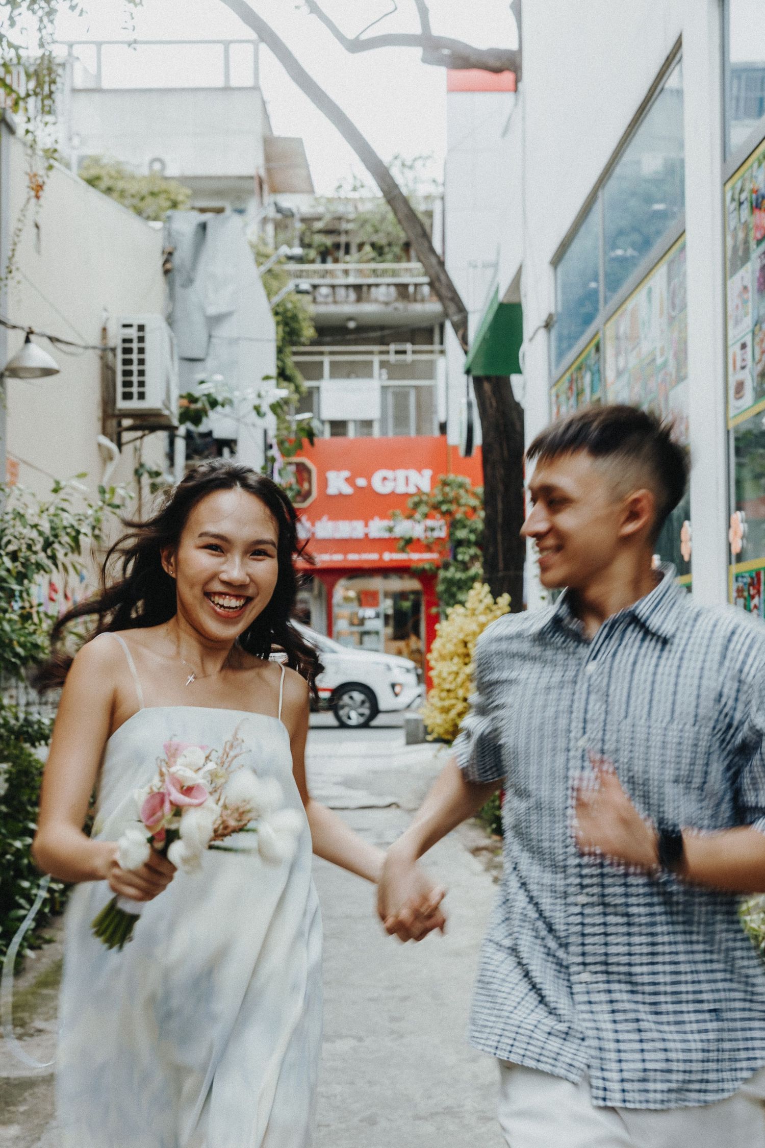 A couple laughs together on a city street with Asian signage visible in the background.