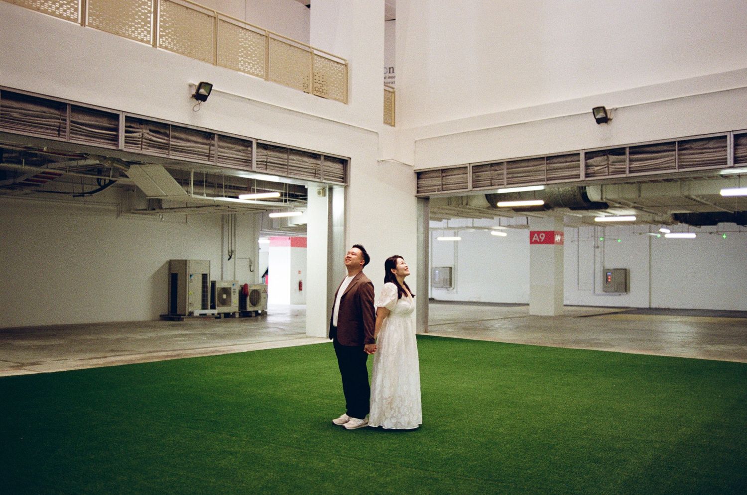 Two people stand on artificial green turf in an industrial indoor space with mirrored walls and exposed ceiling.