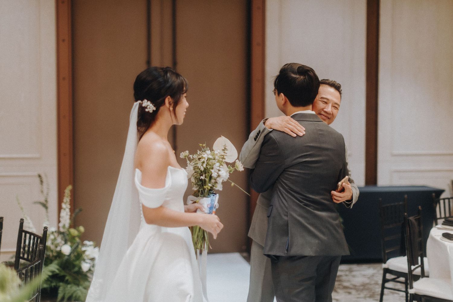 Emotional wedding moment captured during outdoor ceremony with bride in white dress holding bouquet of white flowers.