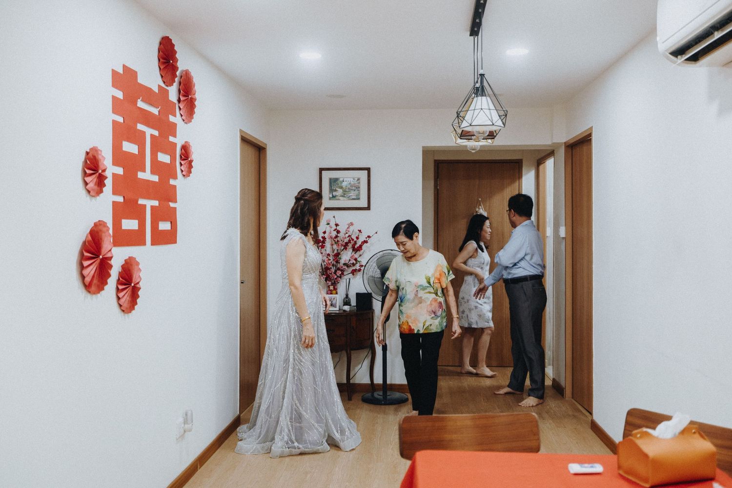 People gather in a bright hallway with white walls and red paper decorations while preparing for a special occasion.