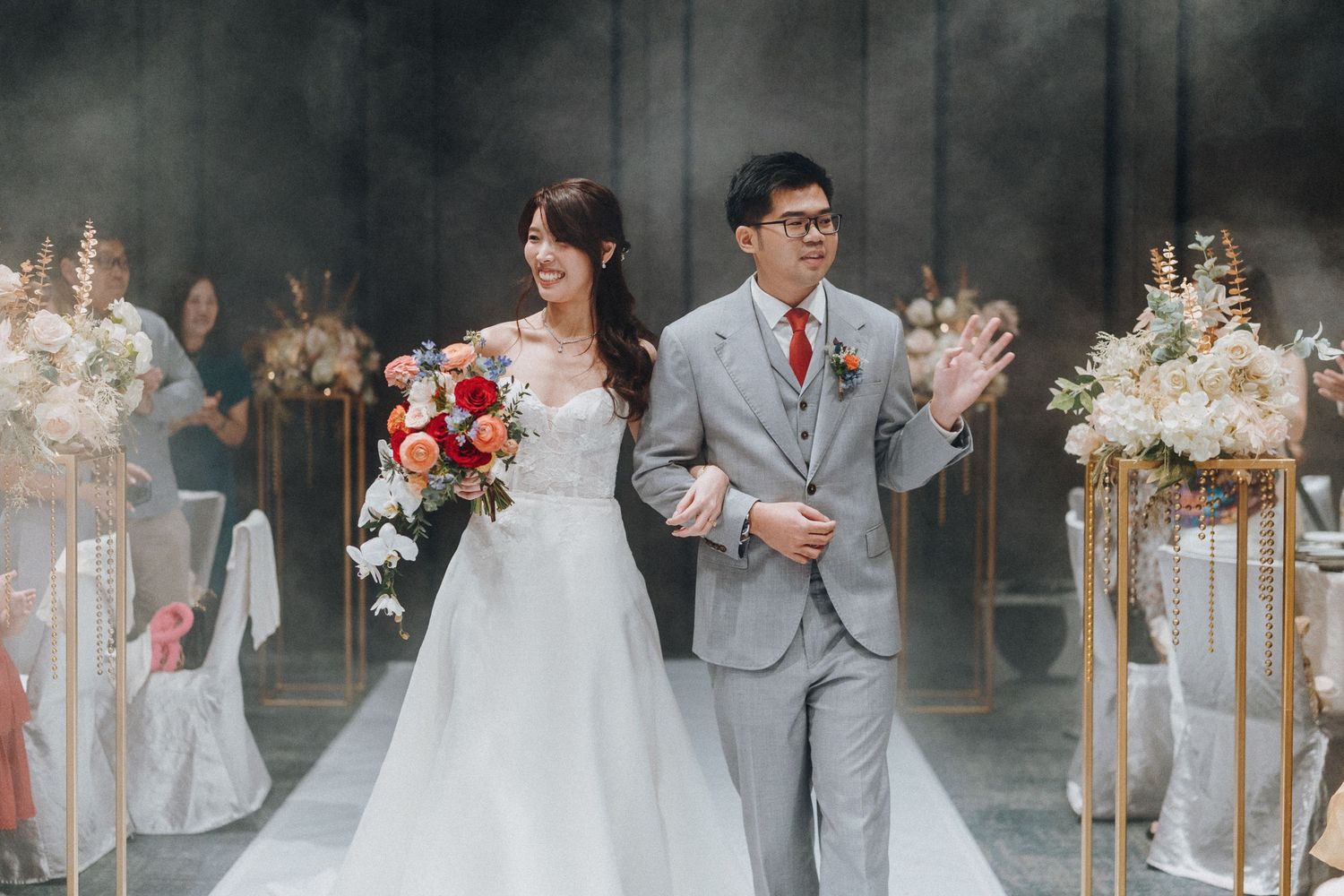The bride and groom walk down the aisle together surrounded by elegant floral arrangements at their wedding ceremony.