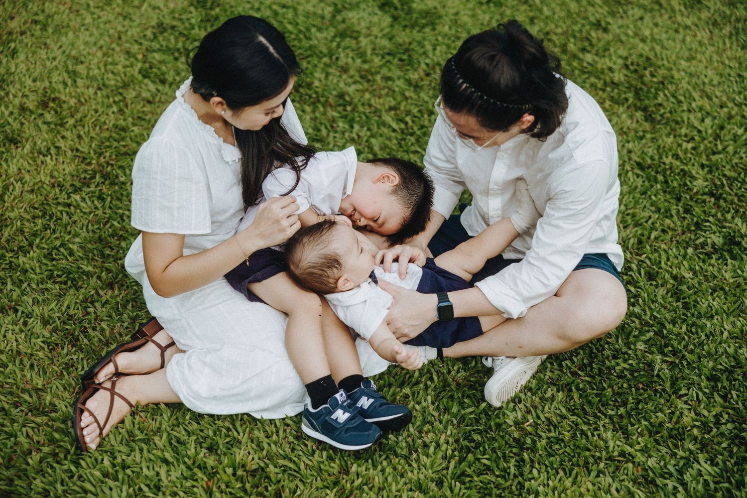 Family spending quality time together while sitting on grass in matching white outfits.