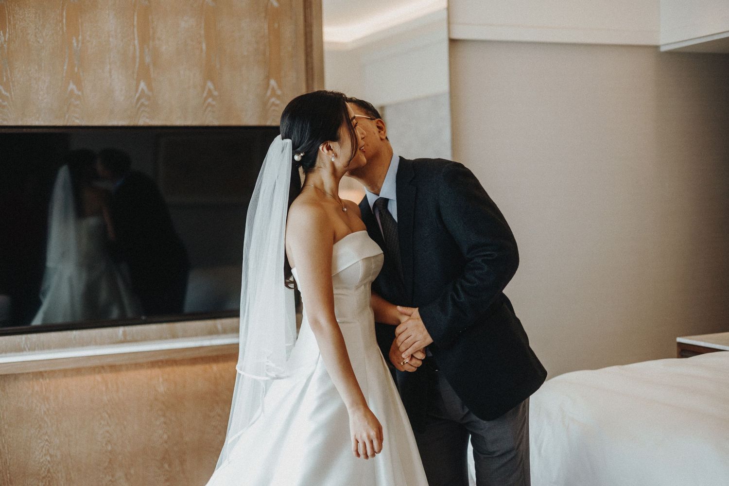 White bridal dress being adjusted in an elegant hotel room with natural lighting.
