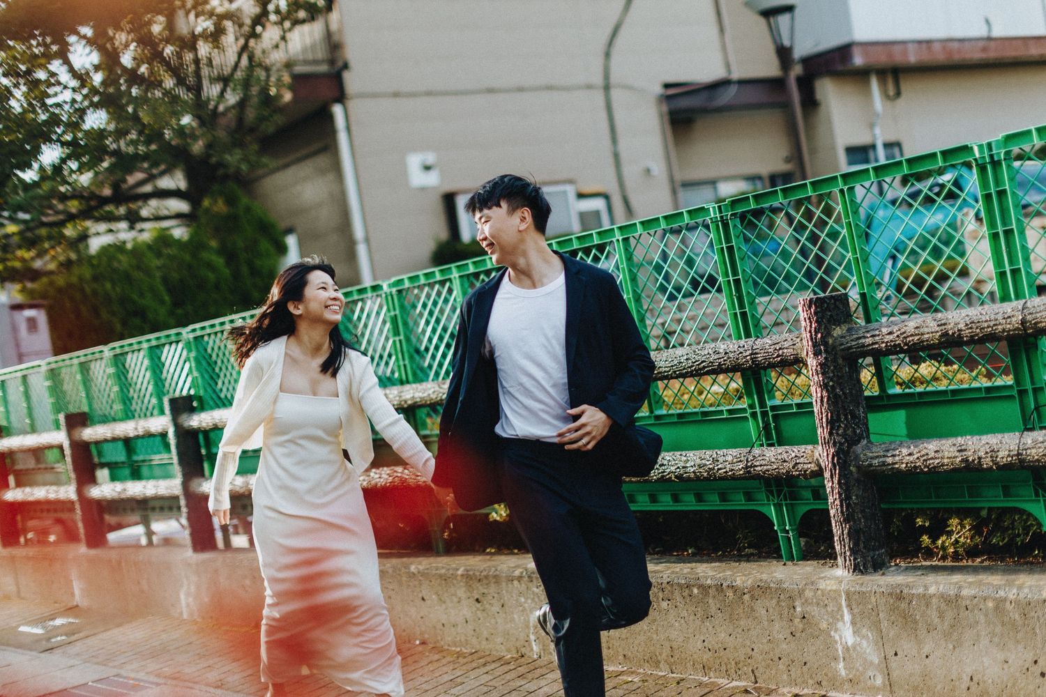 Two people walk together in a playful motion on an outdoor path with green fencing.