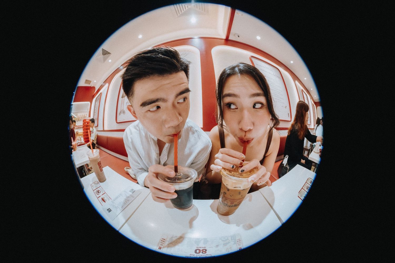Couple sharing drinks through straws captured in a fisheye lens photo at a cozy cafe.