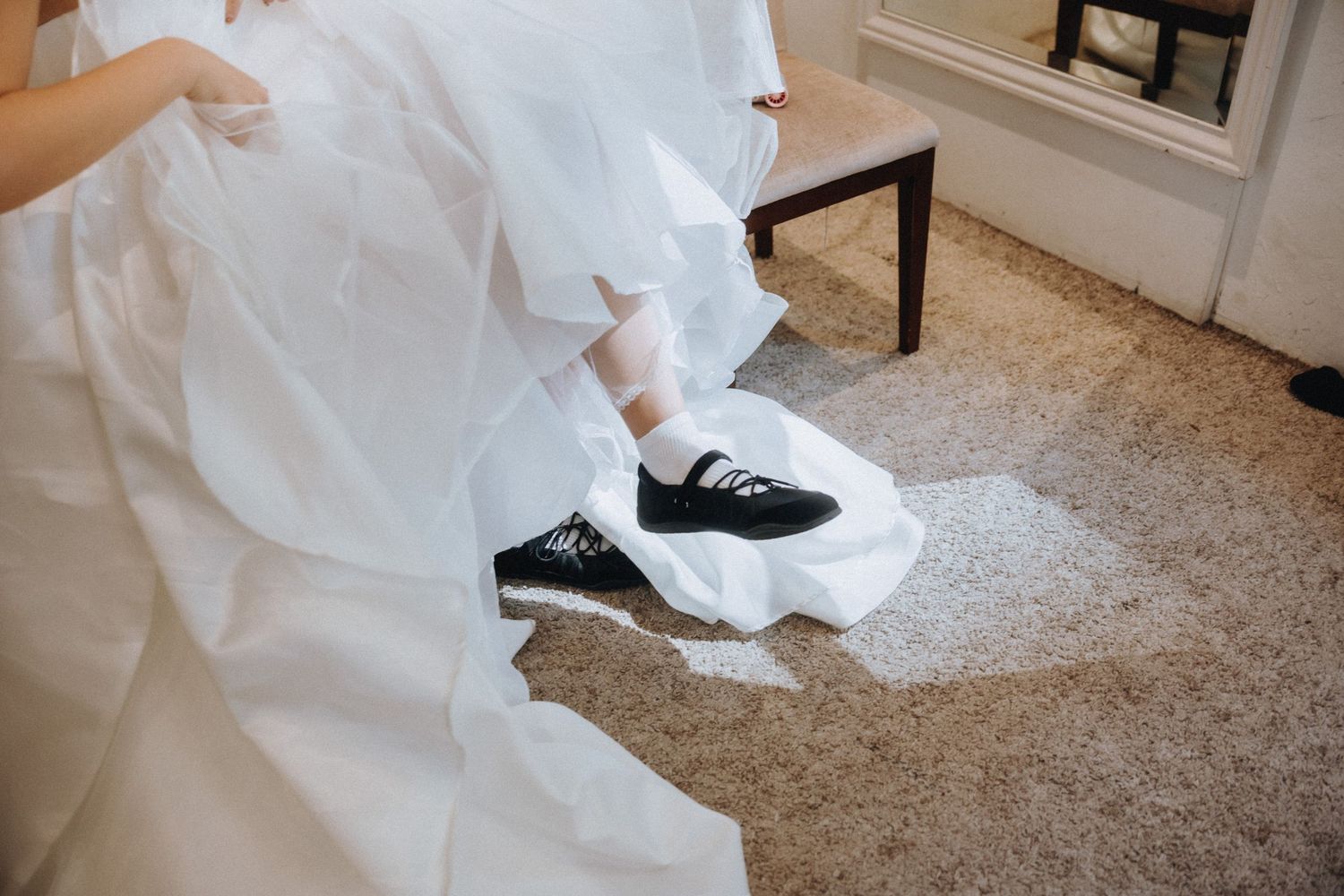 Bride wearing black Vans sneakers under a white wedding dress while seated indoors.